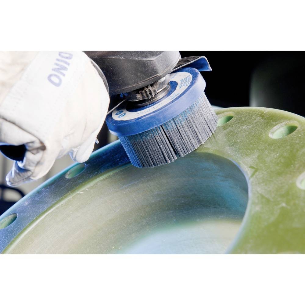 Ein Arbeiter schleift eine grüne Metalloberfläche mit einer elektrischen Schleifmaschine. Die Schutzkleidung ist sichtbar.