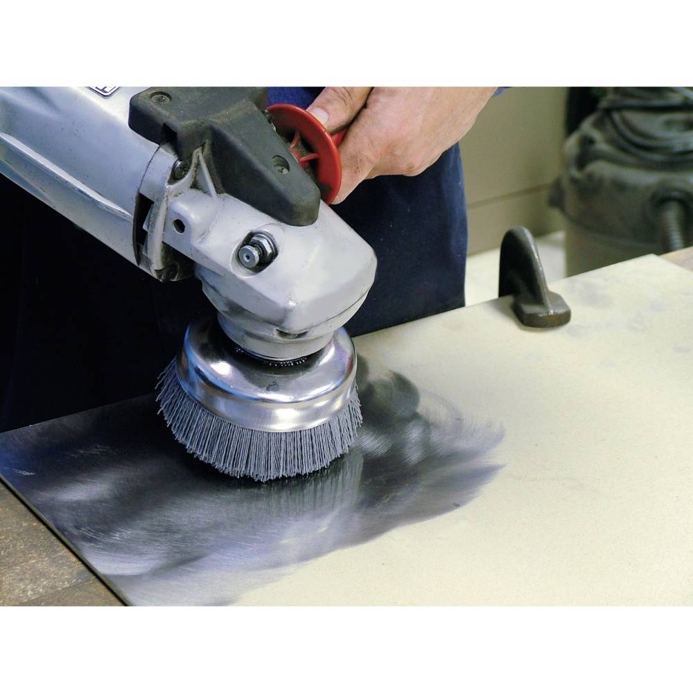 Eine Person schleift mit einer rotierenden Bürste eine Metallplatte, um die Oberfläche zu glätten oder zu reinigen.