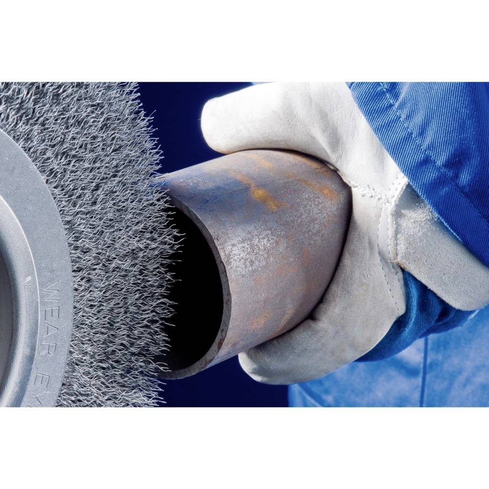 Eine Person in blauer Schutzkleidung hält ein Metallrohr, das mit einer rotierenden Drahtbürste bearbeitet wird.