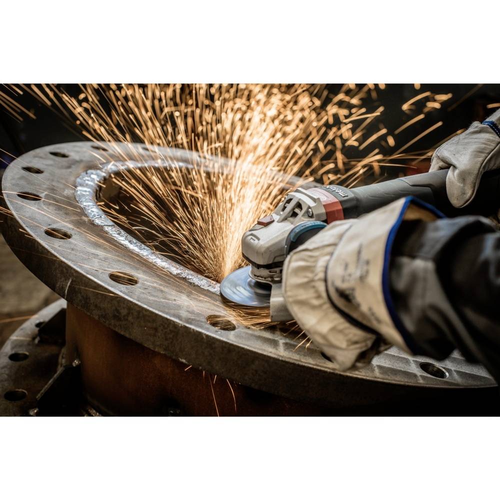 Ein Arbeiter trägt Handschuhe und schleift Funken sprühendes Metall an einer großen rundlichen Metallplatte in einer Werkstatt.