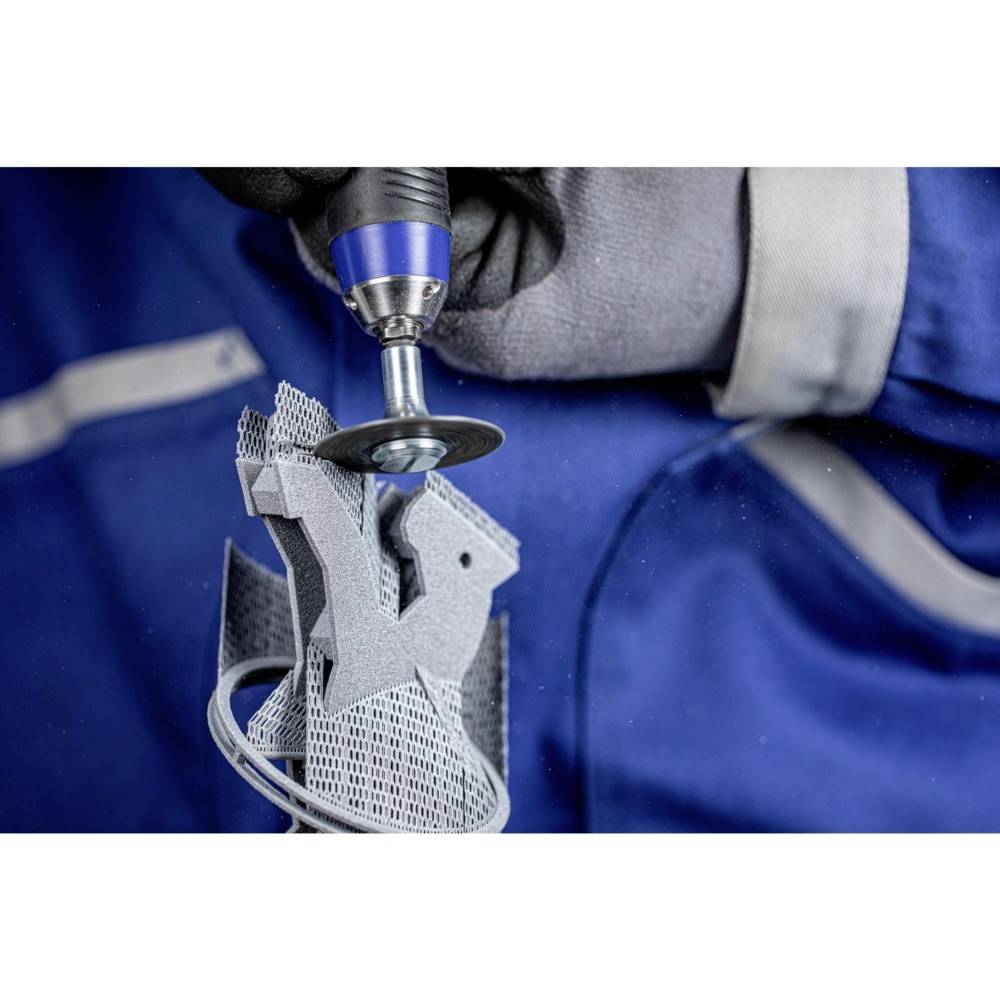 Ein Arbeiter mit Handschuhen schleift eine metallische 3D-gedruckte Struktur mit einem rotierenden Werkzeug ab.