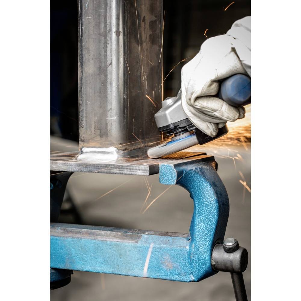 Ein Arbeitshandschuh hält ein Werkzeug, das Funken erzeugt, während es Metall schleift. Eine blau lackierte Metallvorrichtung hält das Werkstück.