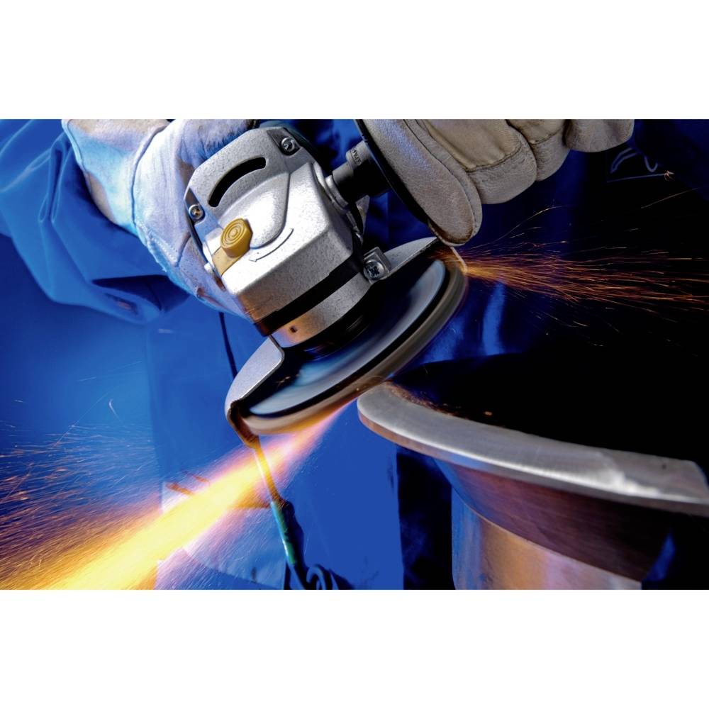 Ein Arbeiter in Schutzkleidung schleift Metall mit einem Winkelschleifer. Funken fliegen in einer Werkstattumgebung.