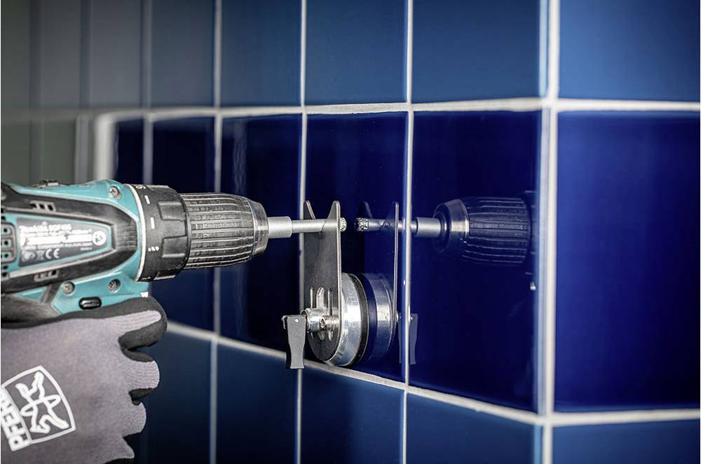 Eine Person bohrt mit einer Bohrmaschine ein Loch in eine dunkelblaue Fliese an einer gefliesten Wand.