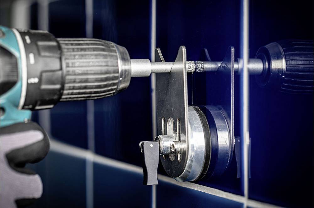 Eine Person verwendet eine Bohrmaschine mit einer speziellen Vorrichtung, um präzise Löcher in eine blaue Fliesenwand zu bohren.