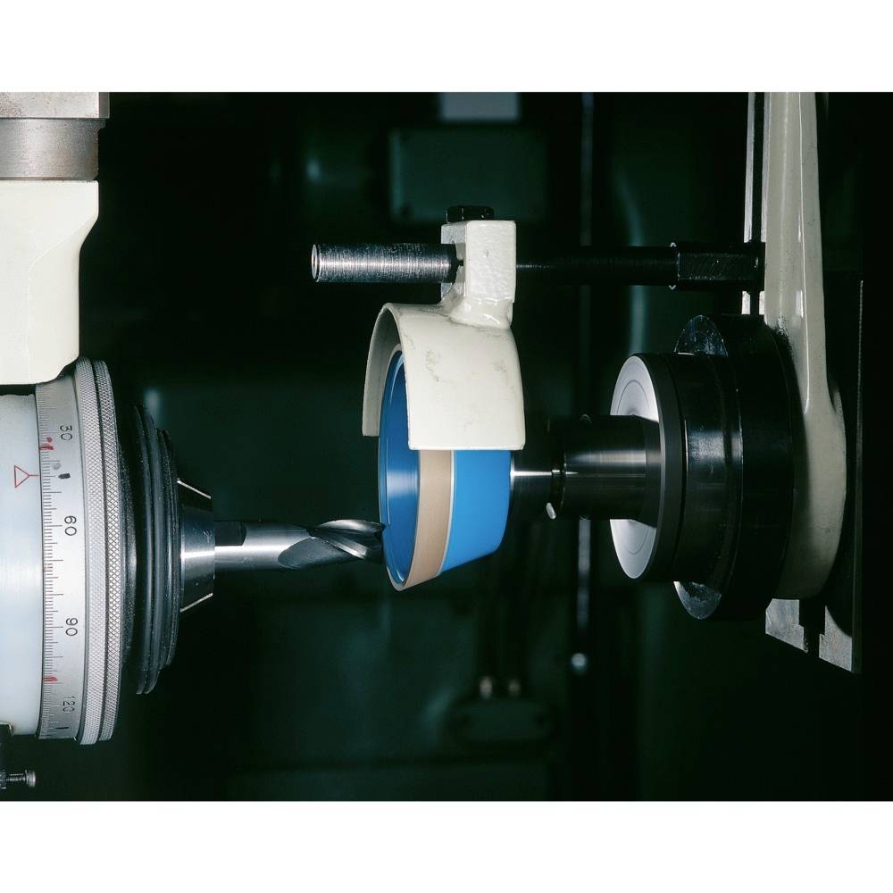 Maschine mit Bohrer, der eine rotierende Scheibe bearbeitet. Nahaufnahme zeigt metallische Präzisionsarbeit in industrieller Umgebung.