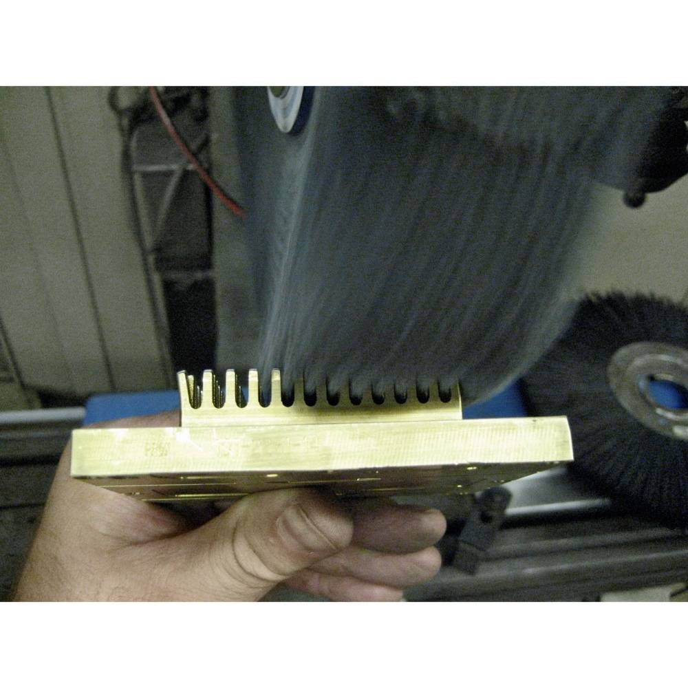 Ein Metallblock wird mit einer rotierenden Schleifscheibe bearbeitet, um Zähne zu formen. Eine Hand hält den Block sicher fest.