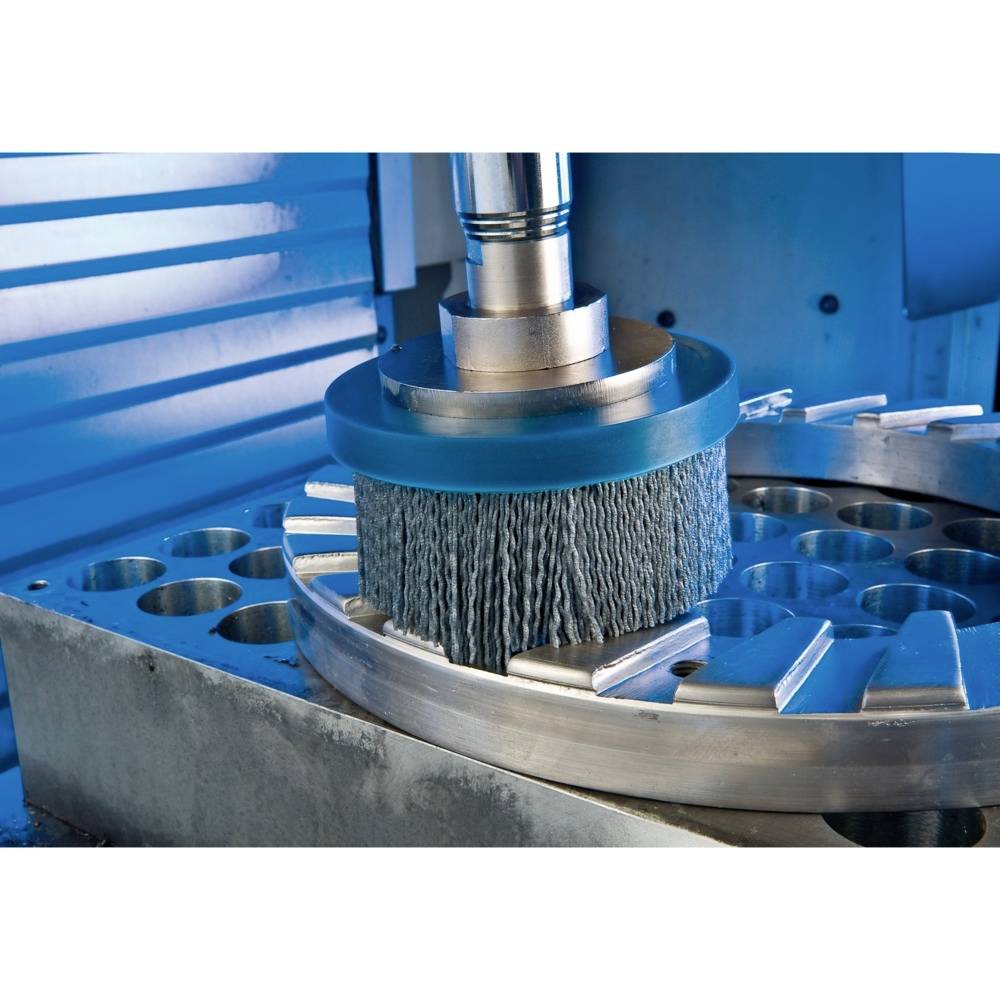 Industrieanlage beim Schleifen von Metall, zeigt einen rotierenden Schleifkopf in Aktion, umgeben von silbern glänzenden Metallteilen.