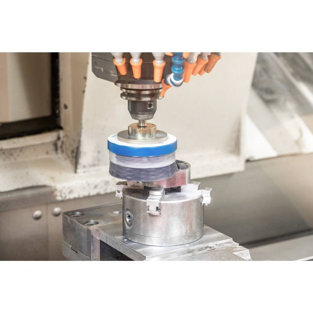Eine CNC-Maschine führt mit einer rotierenden Scheibe einen Polierprozess an einem Metallteil durch, in einer Werkstattumgebung.