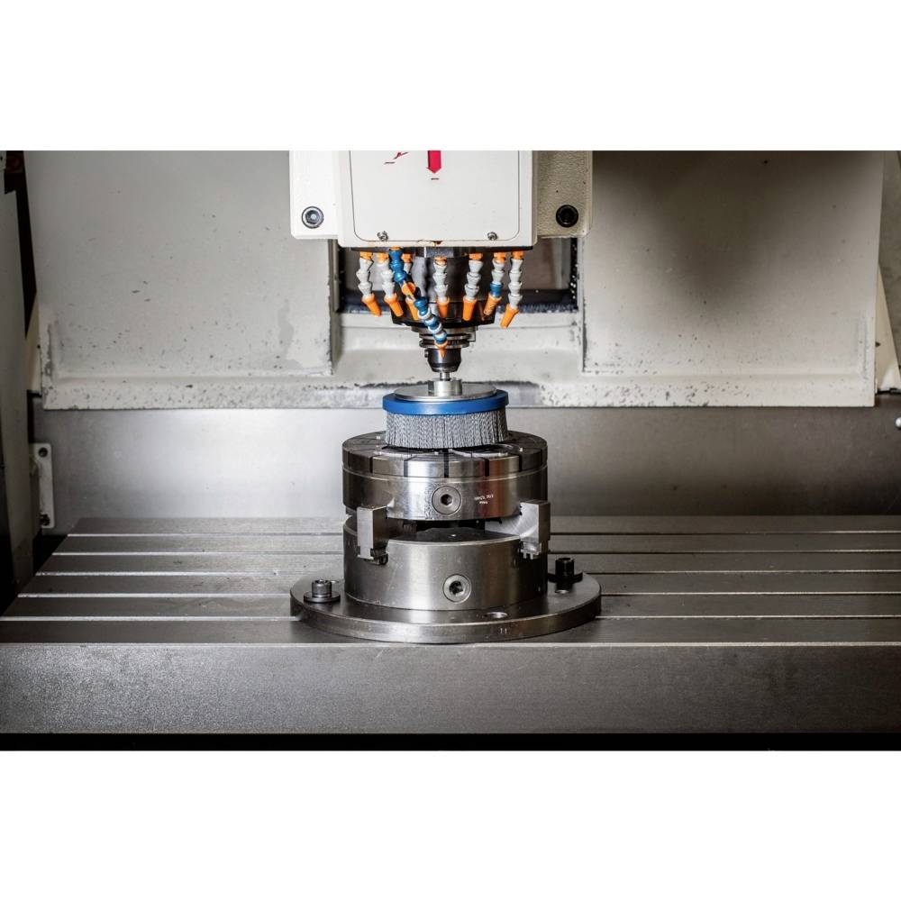 CNC-Maschine bearbeitet Metallteil in einer Werkstatt. Bohrer über rundem Werkstück, umgeben von Kühlmitteldüsen.