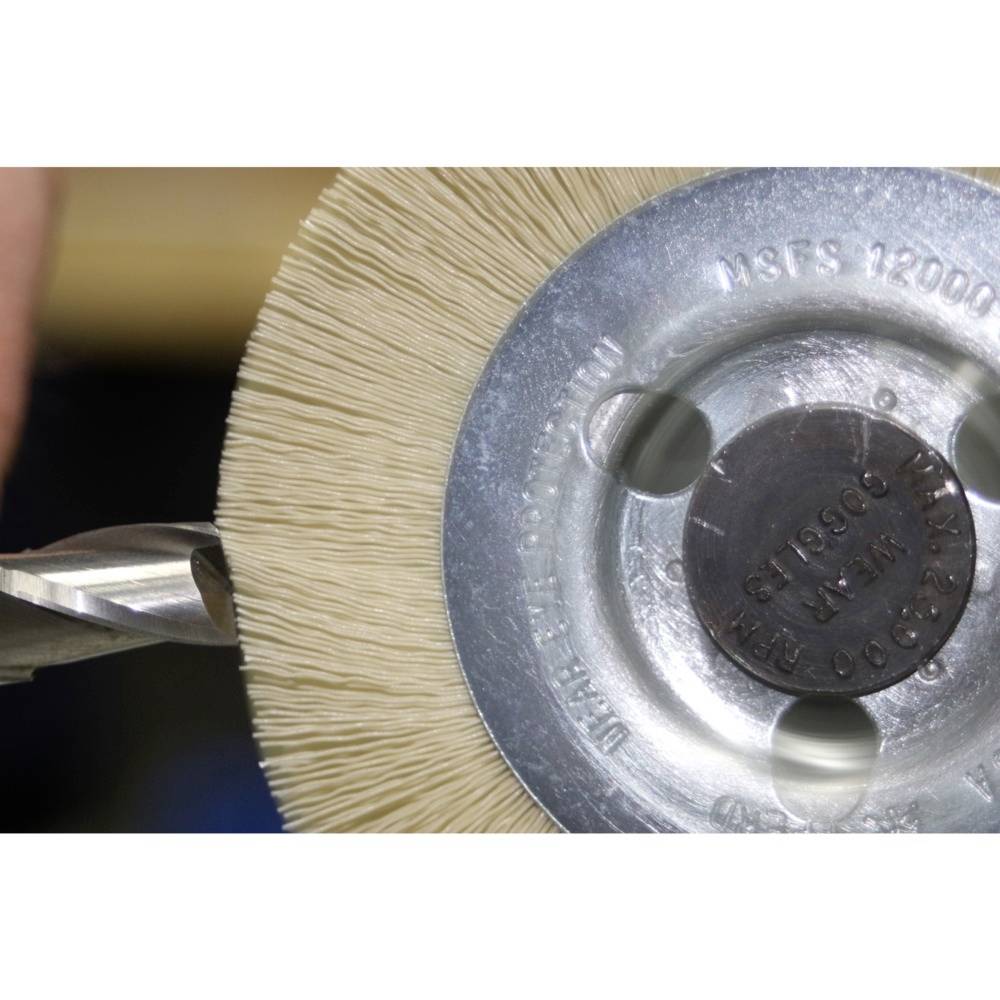 Nahaufnahme einer rotierenden Bürste, die Metall bearbeitet. Ein Bohrer berührt die Bürste, deutet auf Schärfen oder Polieren hin.