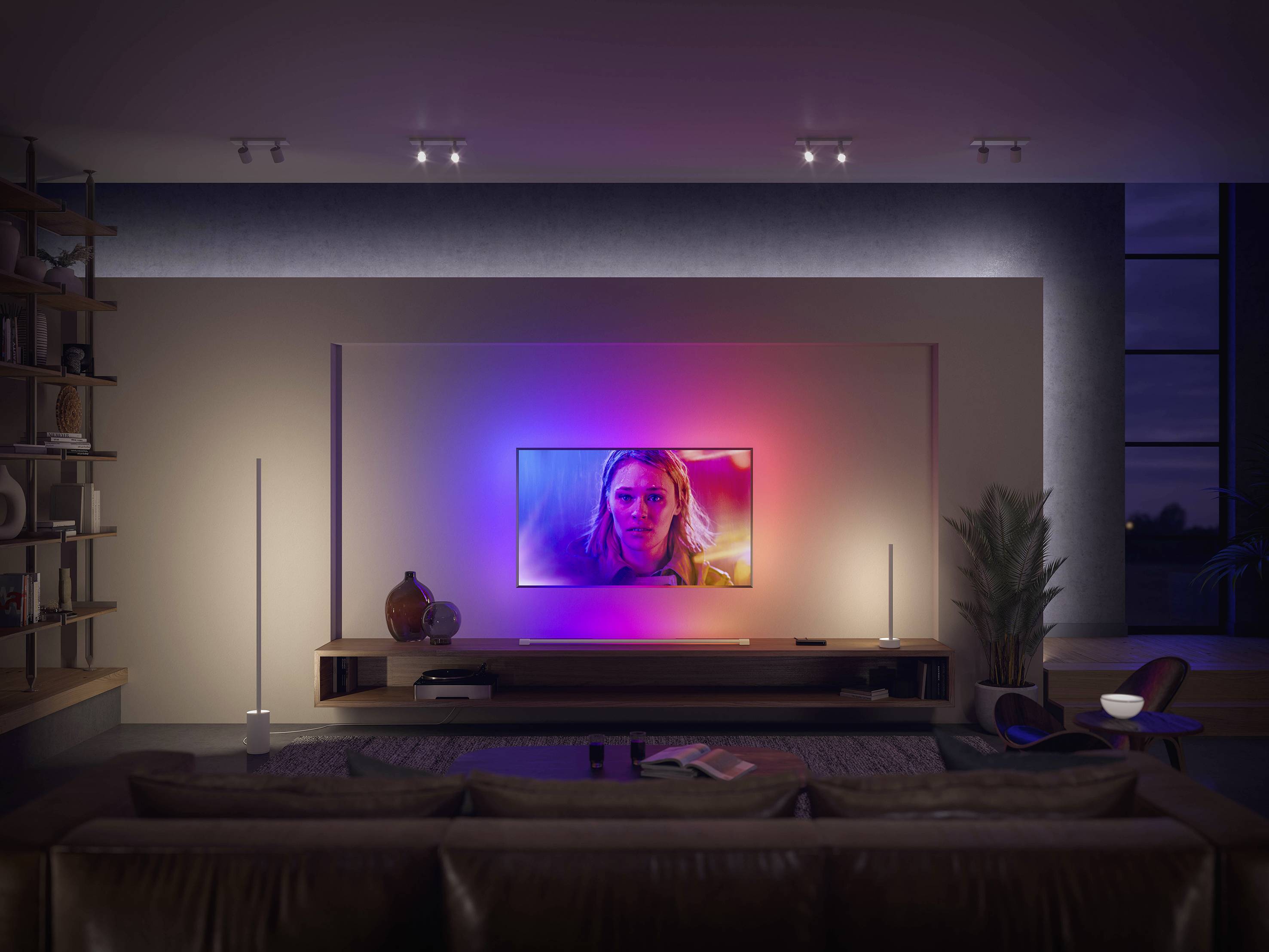 Ein Wohnzimmer mit einem großen Fernseher an der Wand, der eingeschaltet ist. Der Raum ist modern eingerichtet und sanft beleuchtet.