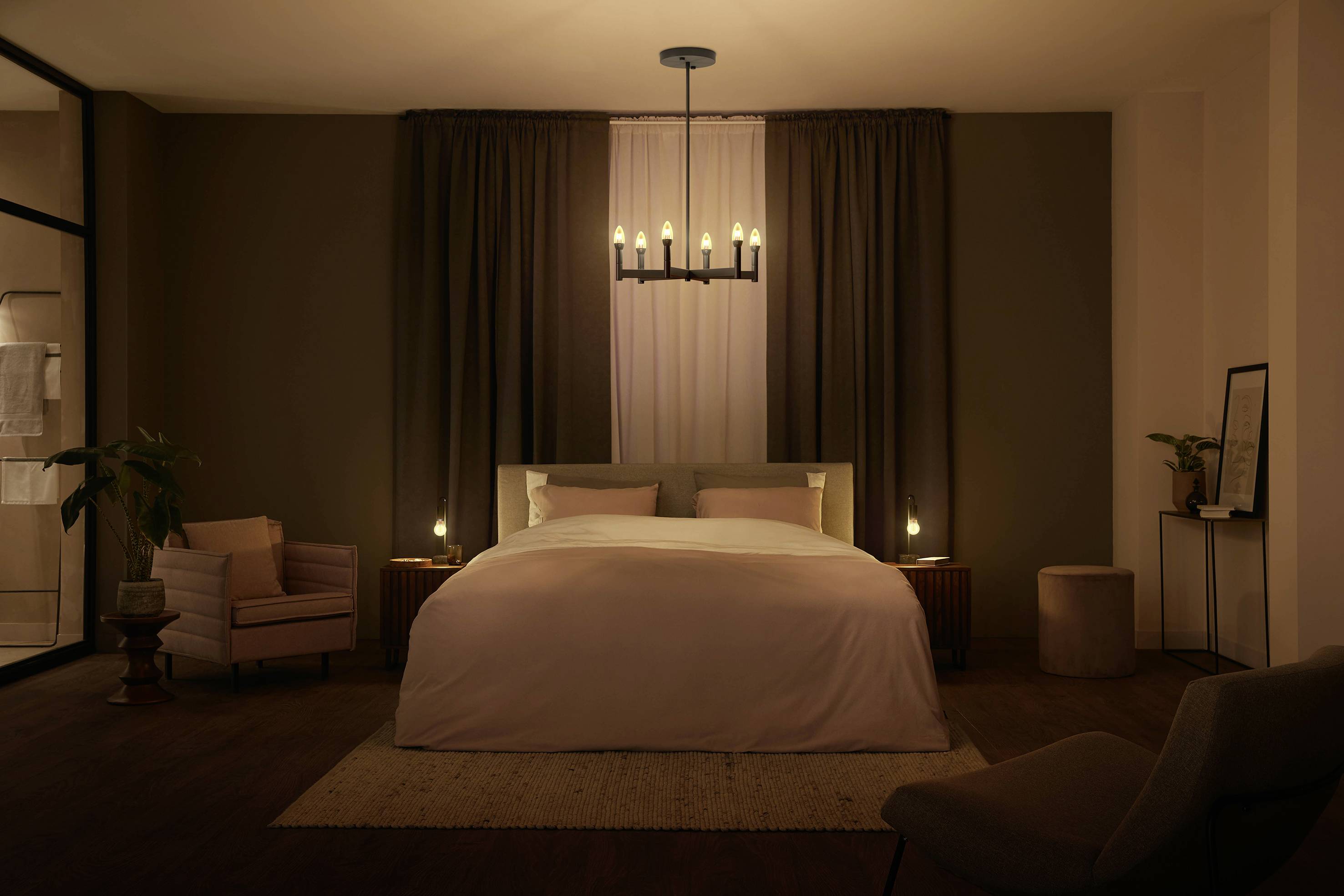 Ein gemütliches Schlafzimmer mit einem großen Bett, flankiert von Nachttischen und Lampen. Eine prunkvolle Hängelampe beleuchtet den Raum.