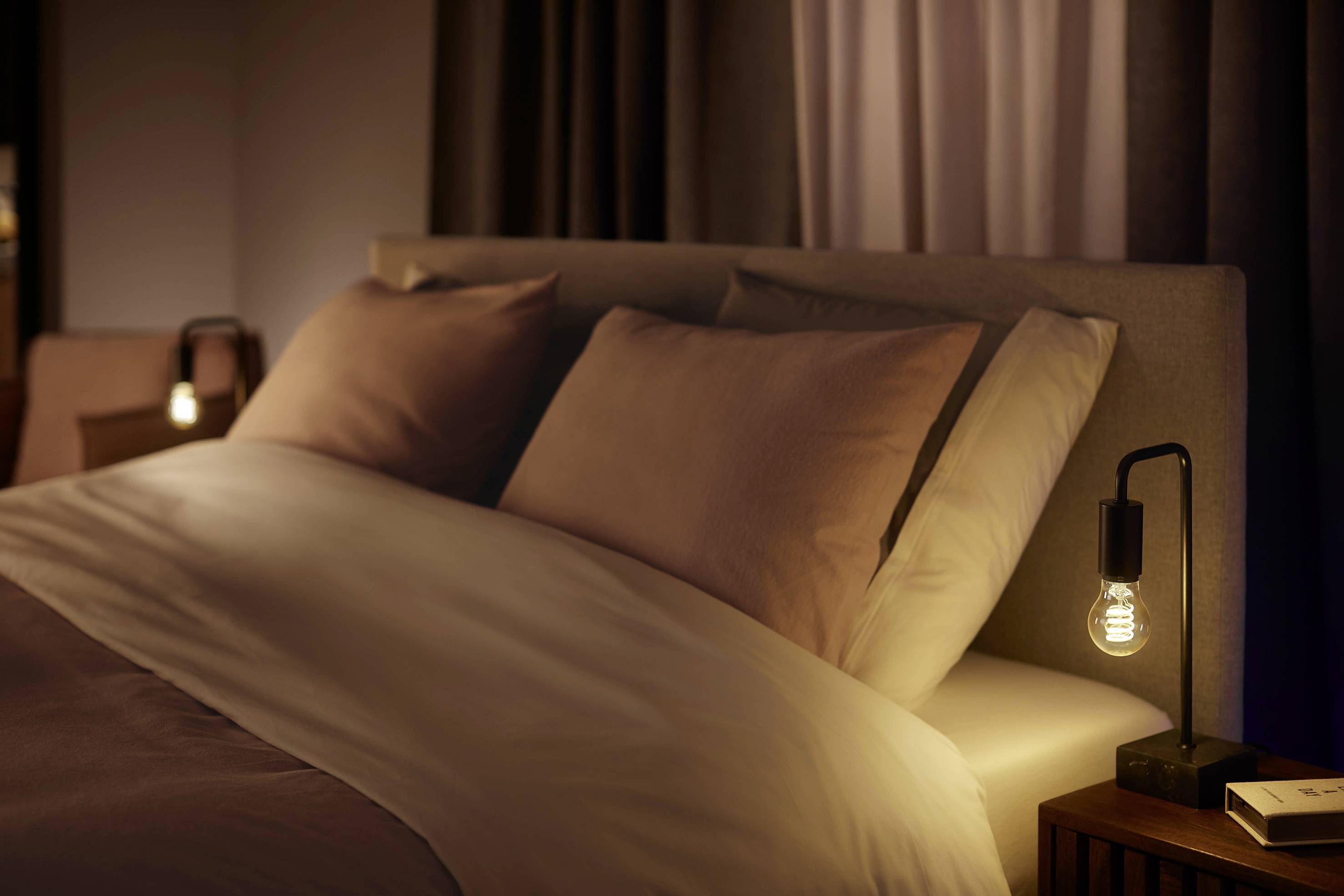 Ein gemütliches Schlafzimmer mit einem großen Bett, zwei Kissen und weicher Beleuchtung von Nachttischlampen.
