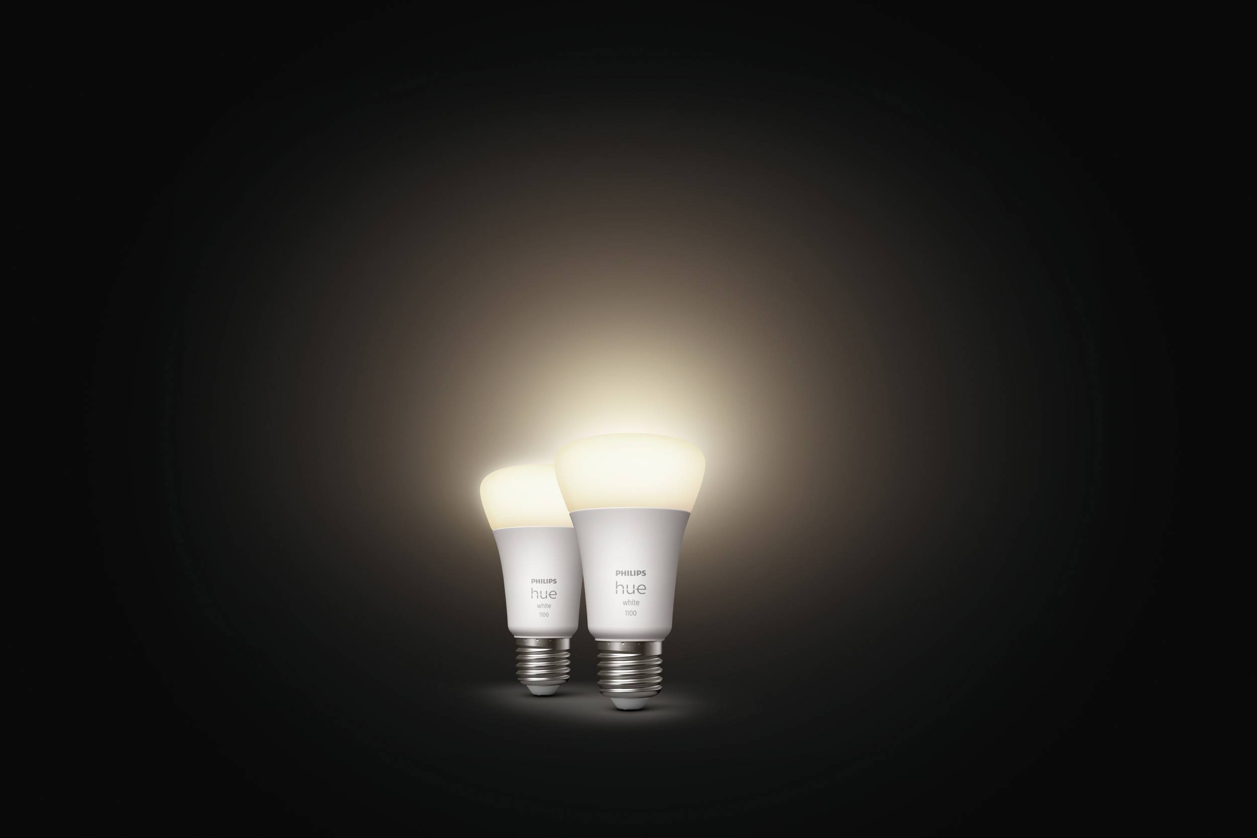 Zwei leuchtende Glühbirnen auf dunklem Hintergrund, die unterschiedliche Helligkeitsstufen zeigen. Hauptsächlich warmweißes Licht.