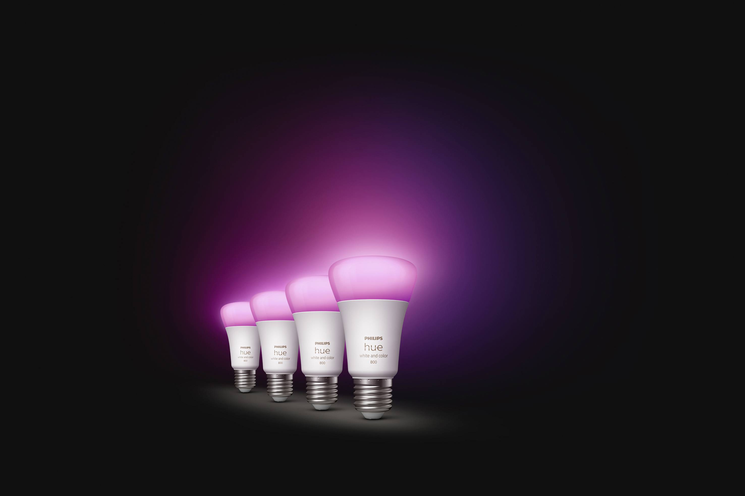 Vier smarte LED-Glühbirnen mit pinkem Leuchten auf dunklem Hintergrund, in einer Reihe angeordnet, erzeugen eine stimmungsvolle Atmosphäre.