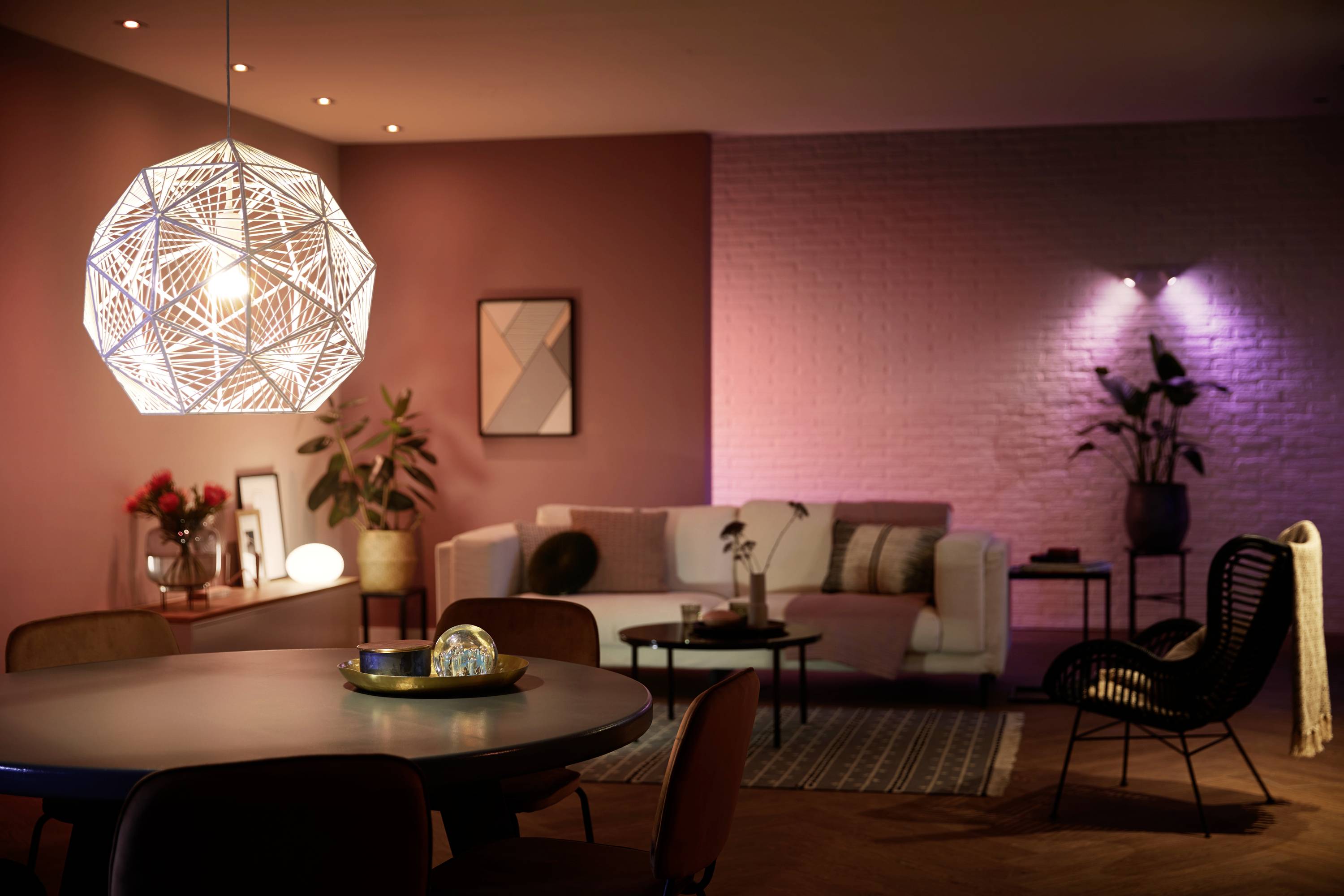 Gemütliches Wohnzimmer mit moderner Hängelampe, beigem Sofa, Dekorationen und gedämpfter Beleuchtung. Atmosphäre wirkt einladend.