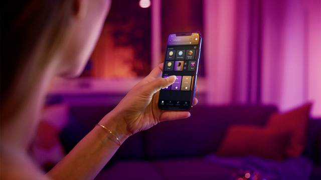 Eine Person bedient ein Smartphone in einem stimmungsvoll beleuchteten Raum. Auf dem Bildschirm sind mehrere Apps zu sehen.