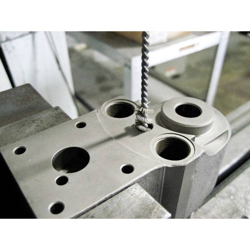 Bohren eines Metallstücks in einer Werkstatt. Ein Bohrer befindet sich über dem Werkstück, das in einer Werkbank eingespannt ist.