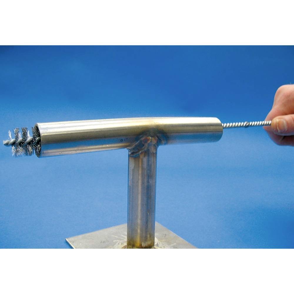 Eine Hand hält eine Metallbürste, die in ein T-förmiges Metallrohr eingeführt wird. Die Bürste reinigt das Innere des Rohrs.