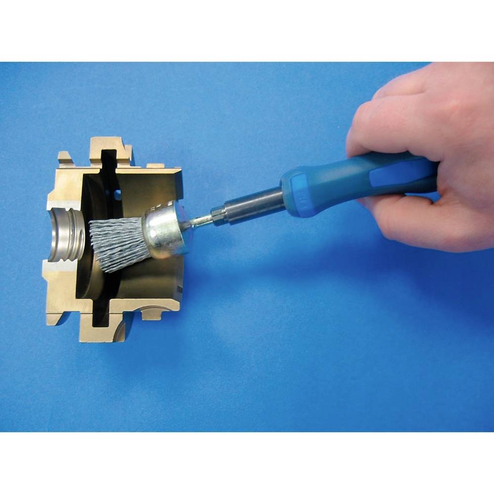 Eine Hand hält ein Werkzeug und reinigt ein metallisches Bauteil mit einer Bürste. Hintergrund ist blau.