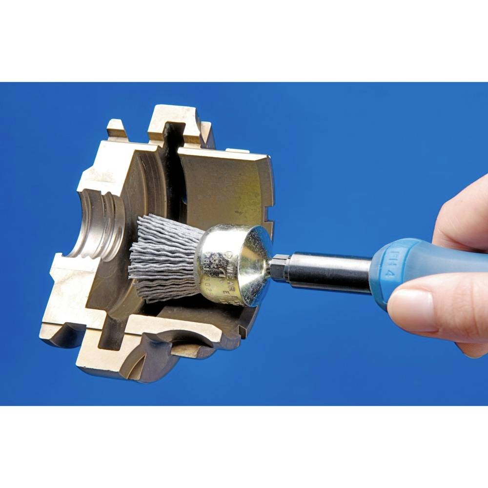Ein Handwerkzeug mit einer runden Drahtbürste poliert das Innere eines mechanischen Teils. Eine Hand hält das Werkzeug.