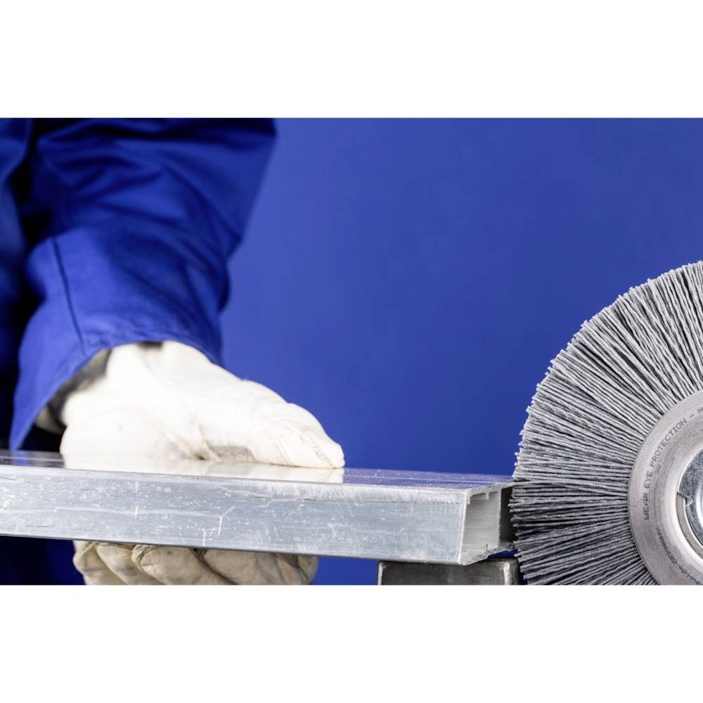 Eine Person in blauer Arbeitskleidung und weißen Handschuhen schleift eine Metallplatte mit einer rotierenden Schleifscheibe.