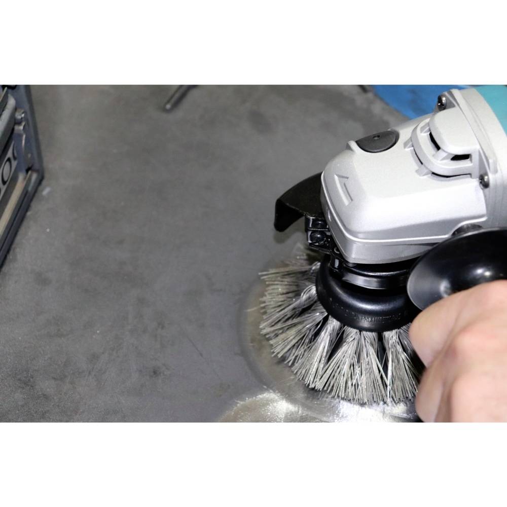 Eine Hand hält eine Elektrobürste, die eine Metalloberfläche reinigt. Staub wird sichtbar weggebürstet.