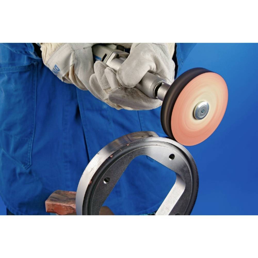 Ein Arbeiter in blauer Kleidung und Handschuhen schleift ein metallisches Werkstück mit einer rotierenden Schleifscheibe.