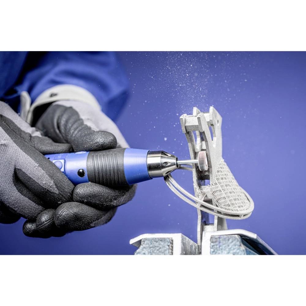 Eine Person bearbeitet eine Metallkomponente mit einem blauen, elektrischen Schleifgerät. Funken fliegen beim Schleifen, Hintergrund ist blau.