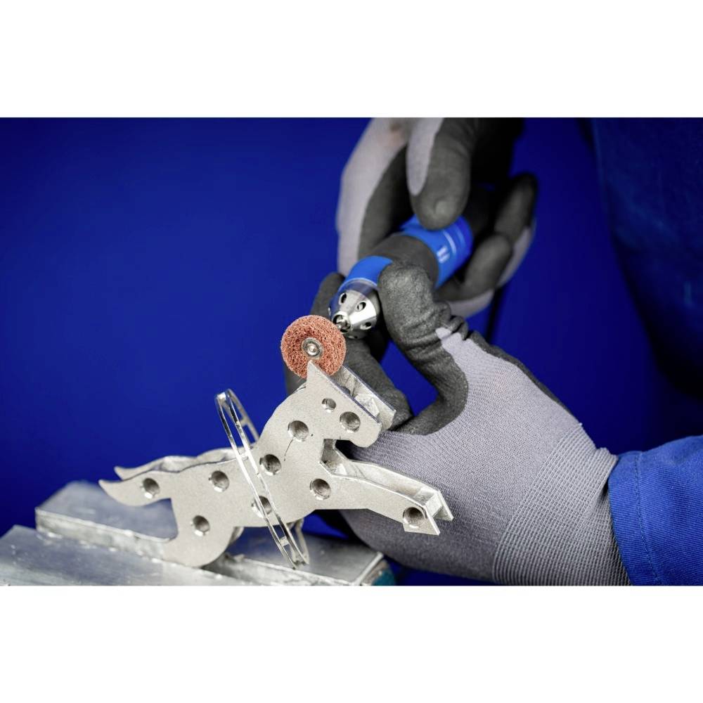 Person glättet eine Metallfigur mit einem rotierenden Schleifwerkzeug; trägt Handschuhe. Blaue Schutzkleidung.