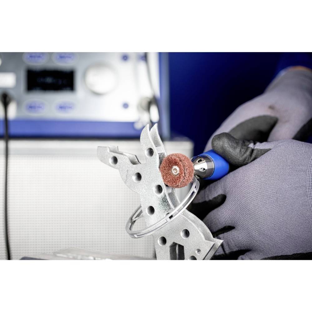 Eine Person trägt Handschuhe und verwendet ein elektrisches Werkzeug, um ein Metallteil mit einer rotierenden Scheibe zu polieren.