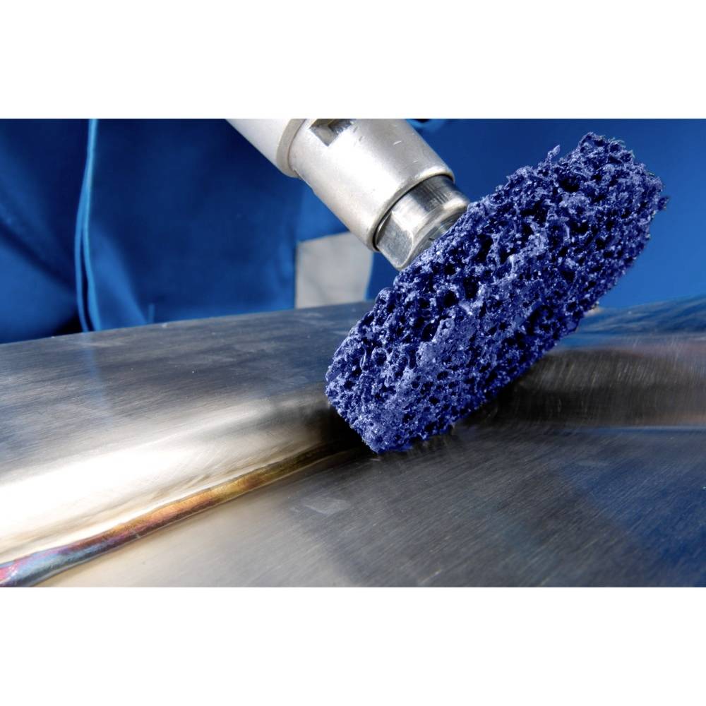 Eine blaue Reinigungsbürste wird über eine metallische Oberfläche geführt. Eine Person in blauer Kleidung hält das Werkzeug.