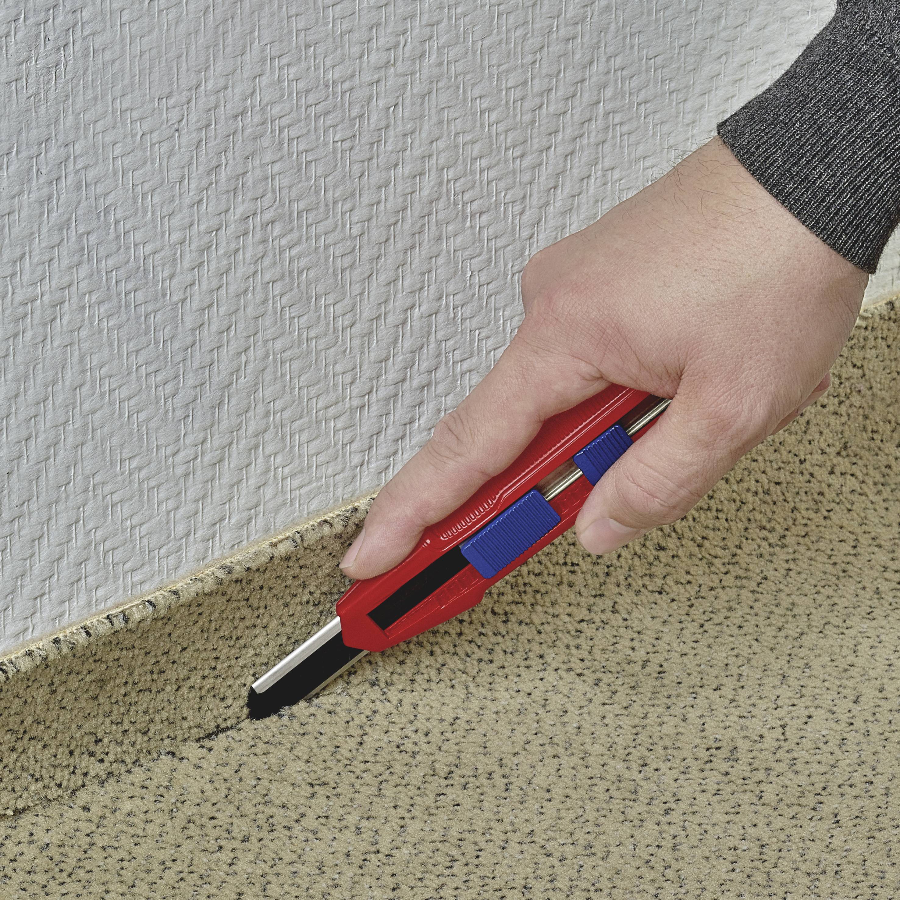 Eine Hand schneidet mit einem Teppichmesser Teppichboden entlang einer Kante. Der Teppich hat eine beigefarbene Textur.