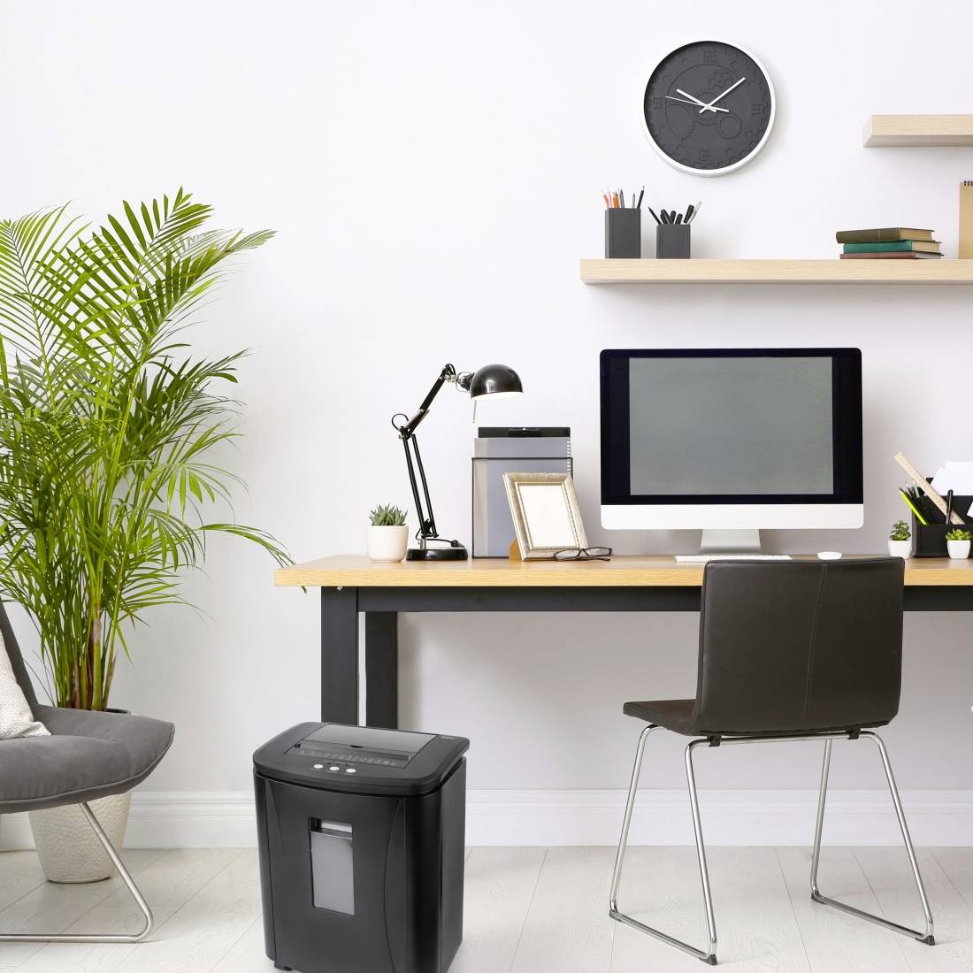 Ein gemütliches Home-Office mit einem Tisch, darauf ein Computer, Lampe und Pflanzen. An der Wand eine Uhr und Regale. Ein Papierkorb steht auf dem Boden.