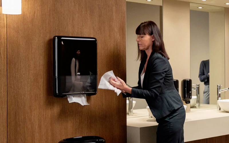 Frau entnimmt Papiertücher aus einem Spender in einem modernen Badezimmer.