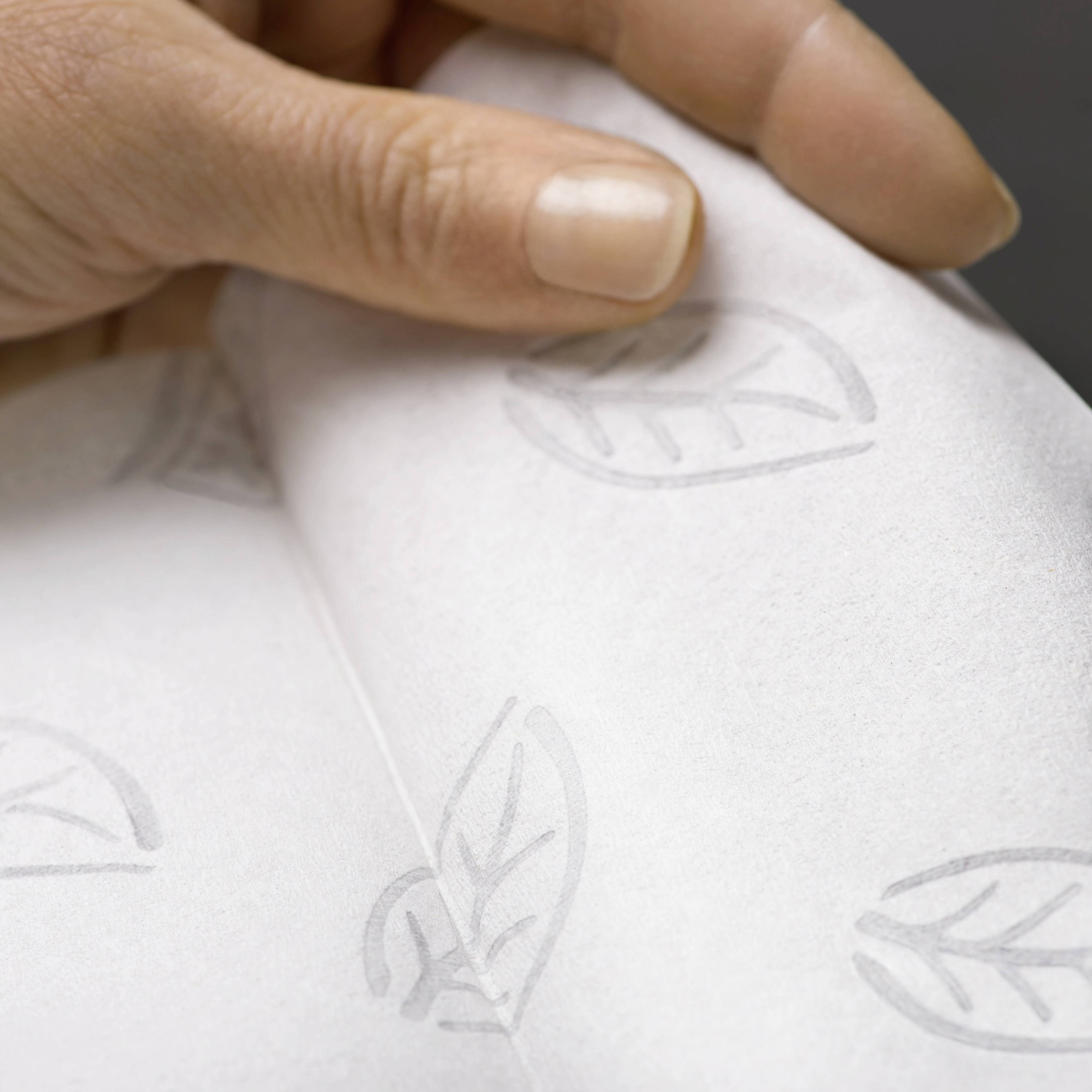 Eine Hand hält ein Stück weißes Papier mit einem dezenten Blattmuster, was auf Umweltfreundlichkeit hindeutet.