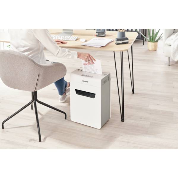 Eine Person sitzt an einem Schreibtisch und zerkleinert ein Papier mit einem Aktenvernichter. Der Raum ist modern eingerichtet.