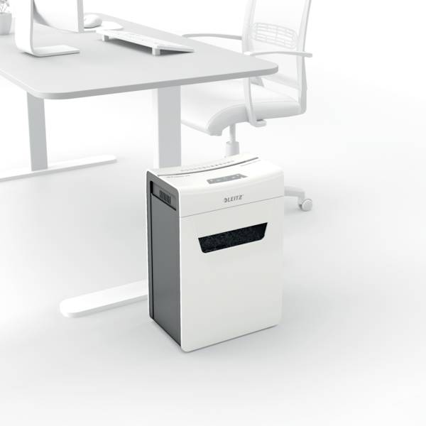 Ein weißer Aktenvernichter neben einem modernen Bürotisch mit Stuhl. Der Aktenvernichter steht bereit für den Einsatz im Büro.