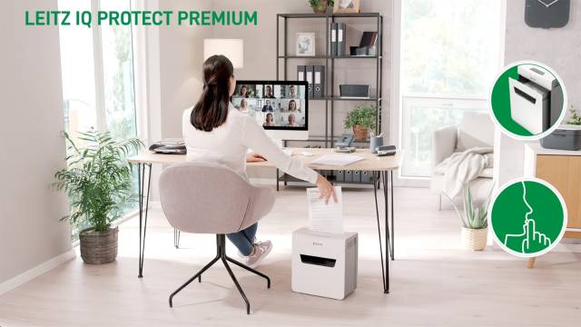 Eine Frau sitzt an einem Schreibtisch, arbeitet am Computer. Im Hintergrund ein Regal, Pflanzen, und ein Aktenvernichter im Vordergrund.