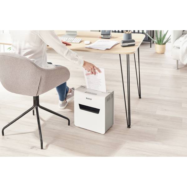 Eine Person sitzt an einem Tisch und benutzt einen Aktenvernichter. Sie zerkleinert ein Blatt Papier in einem modernen Büro, das ordentlich eingerichtet ist.