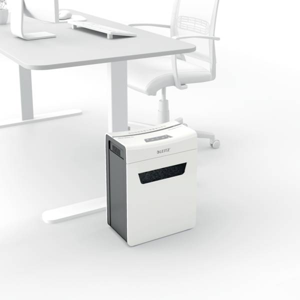 Ein weißer Aktenvernichter steht auf dem Boden neben einem modernen Büroschreibtisch und einem Bürostuhl.