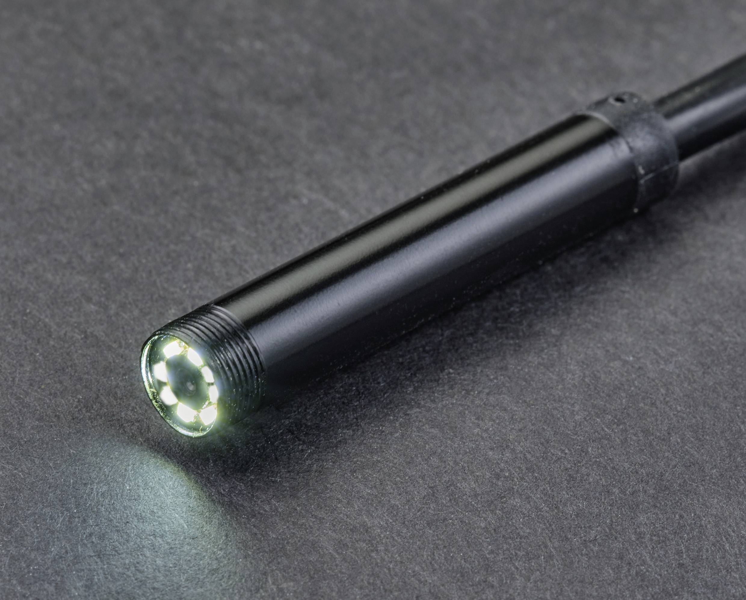 Nahaufnahme eines schwarzen Endoskops mit leuchtenden LED-Lichtern an der Spitze, auf grauem Hintergrund liegend.