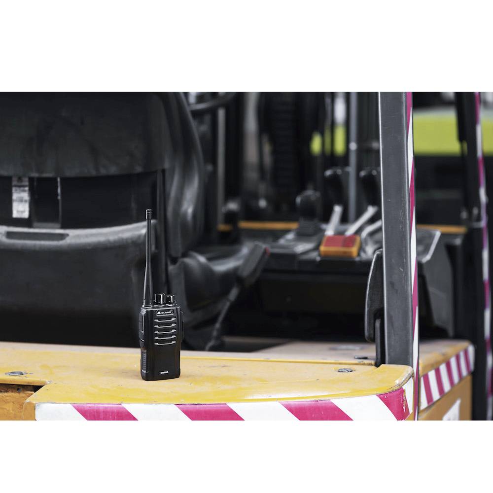 Ein Walkie-Talkie steht auf dem Armaturenbrett eines gelben Fahrzeugs mit Streifenmuster, im Hintergrund sind Bedienelemente erkennbar.