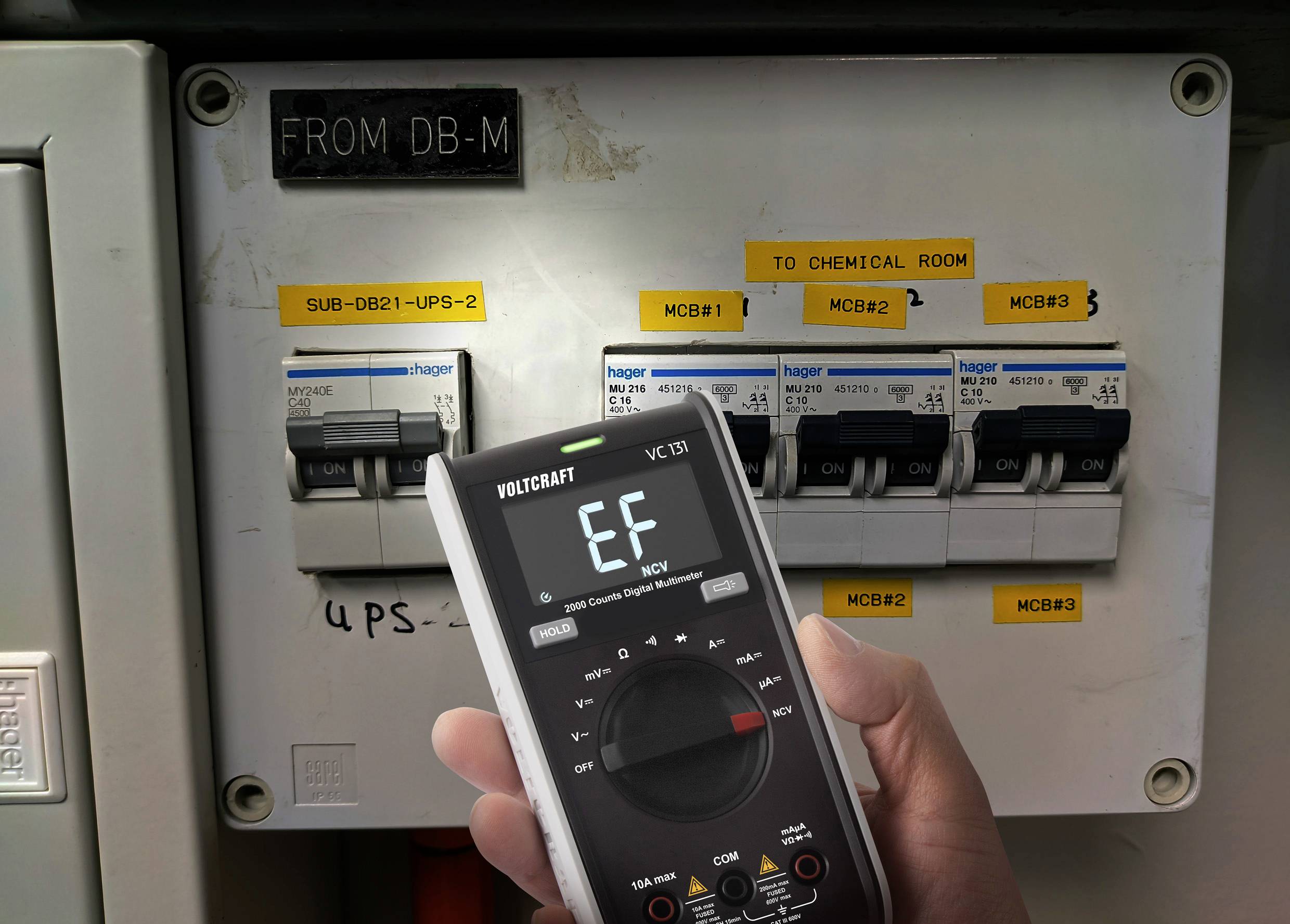 Ein digitales Multimeter zeigt 'EF' an, während es auf einen Schaltschrank mit mehreren Sicherungen gerichtet ist. Schilder zeigen verschiedene Stromkreise an.