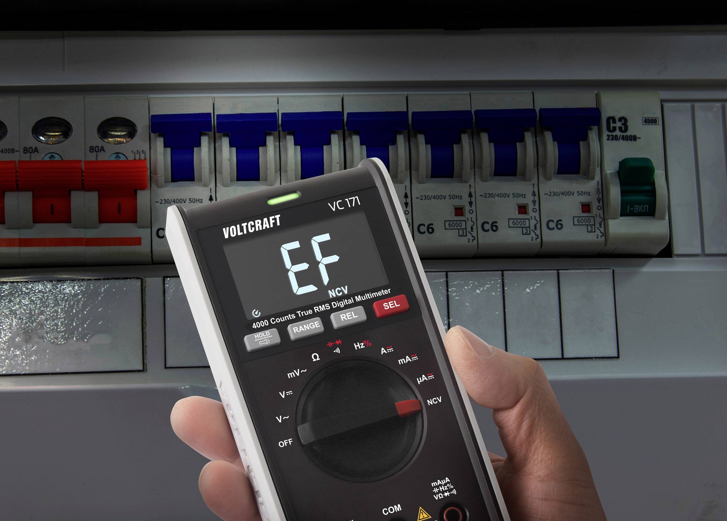 Person hält ein Multimeter in der Hand, das den Fehlercode EF anzeigt. Im Hintergrund ist ein Stromverteilerkasten sichtbar.