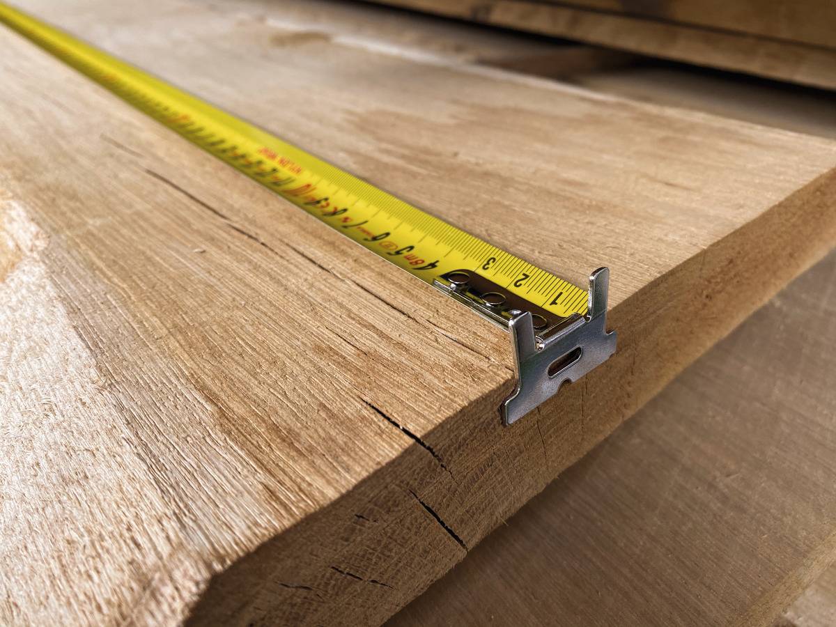 Ein Maßband liegt auf einem Holzbrett, das die Länge misst. Das Brett zeigt eine glatte Oberfläche mit sichtbaren Holzmaserungen.