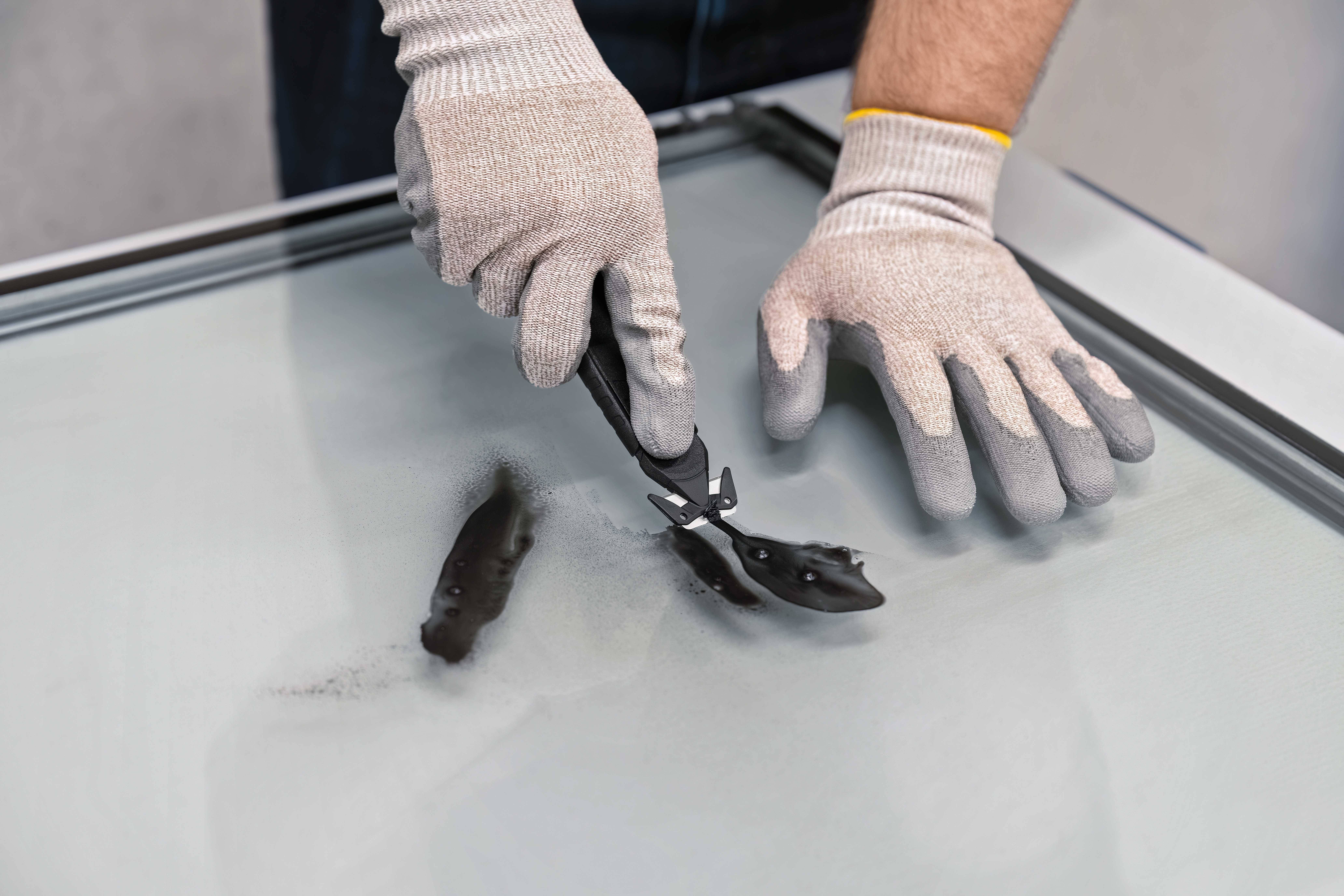 Person mit Handschuhen bearbeitet Glas mit einer Spezialzange. Sicherheit steht im Vordergrund bei der sorgfältigen Glasverarbeitung.