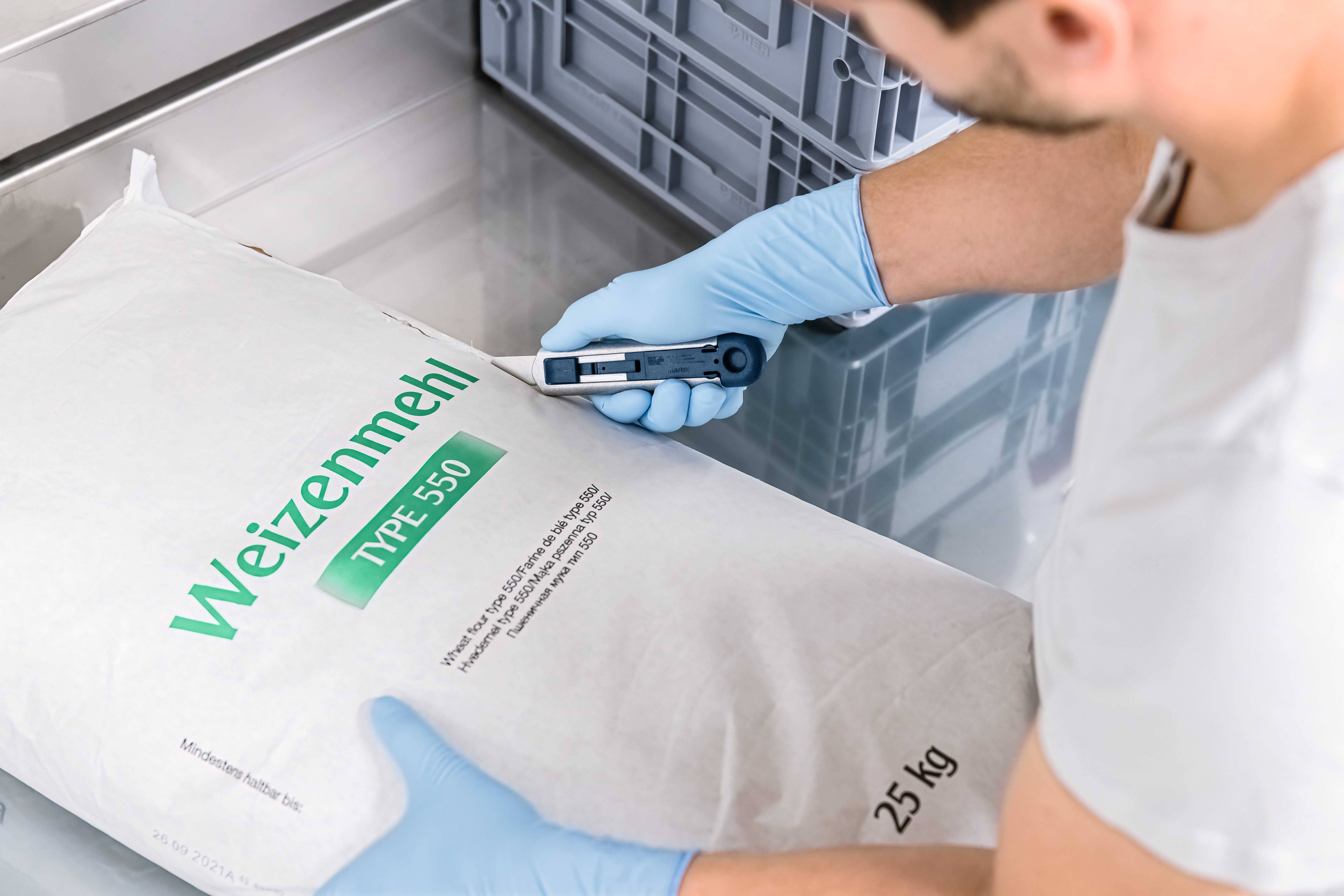Eine Person überprüft mit einem Barcode-Scanner einen 25 kg Sack Weizenmehl Typ 550.