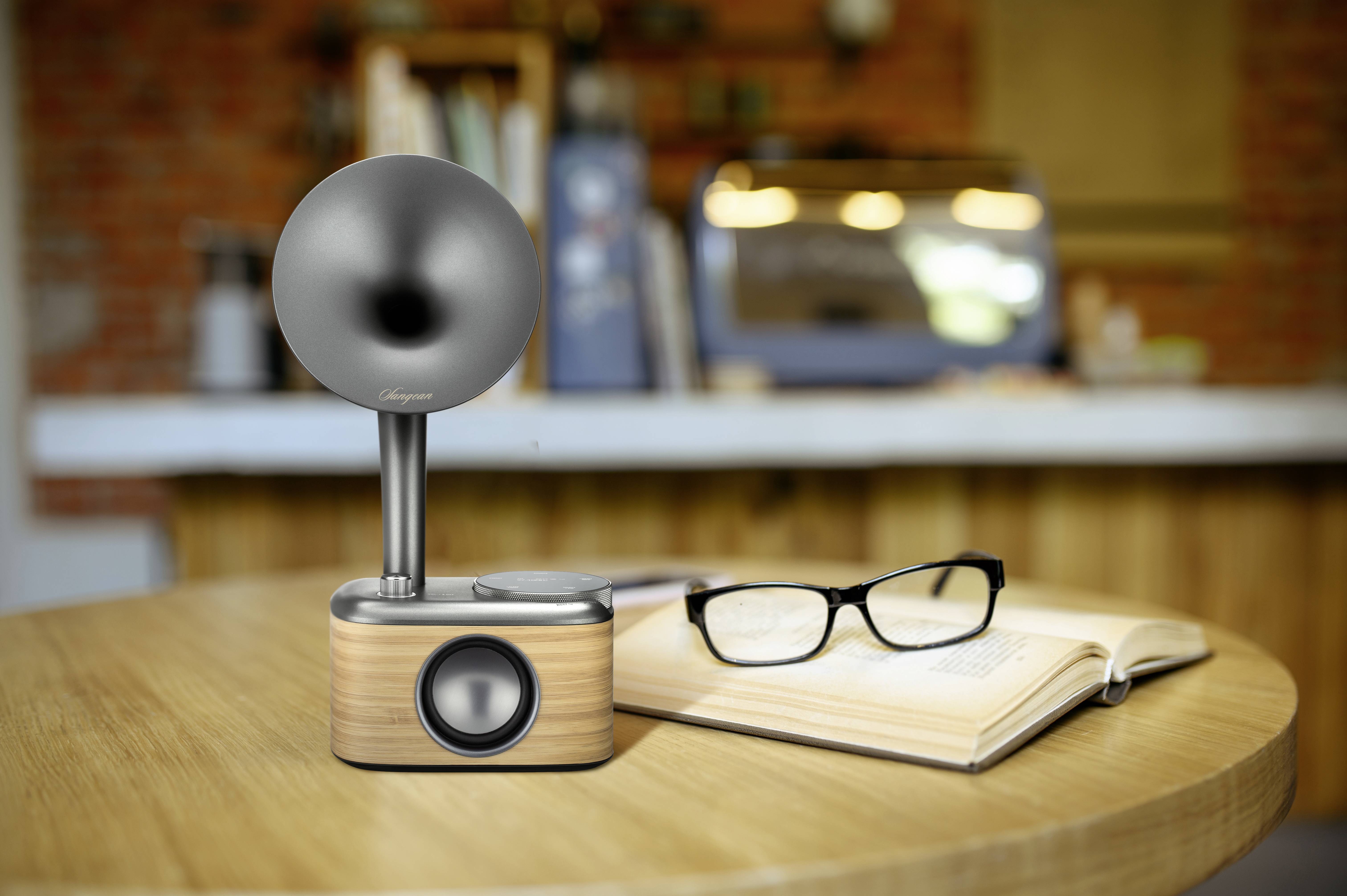 Ein stilvoller Retro-Lautsprecher aus Holz und Metall steht auf einem Tisch neben einer geöffneten Brille und einem aufgeschlagenen Buch.